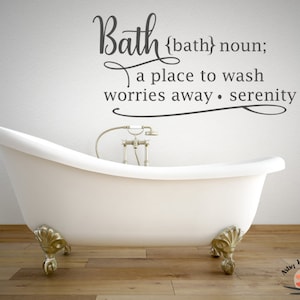 May include: A white bathtub with gold feet and a gold faucet. The text on the wall reads: "Bath {bath} noun; a place to wash worries away. serenity".