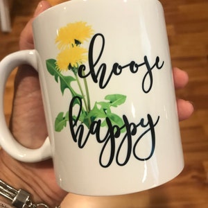 May include: White ceramic mug with a dandelion design and the text "choose happy" in black script.