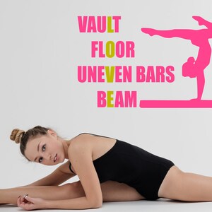 May include: A young woman in a black leotard is stretching on a white background. The words "VAULT", "FLOOR", "UNEVEN BARS", and "BEAM" are written in yellow on the wall. A pink silhouette of a gymnast performing on a balance beam is also on the wall.