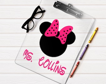 Puede incluir: Un portapapeles de acrílico transparente con una silueta negra de cabeza de ratón y un lazo rosa brillante con puntos. El texto "MS. COLLINS" está impreso en letras rosa brillante debajo de la silueta. Gafas negras y tres ceras.