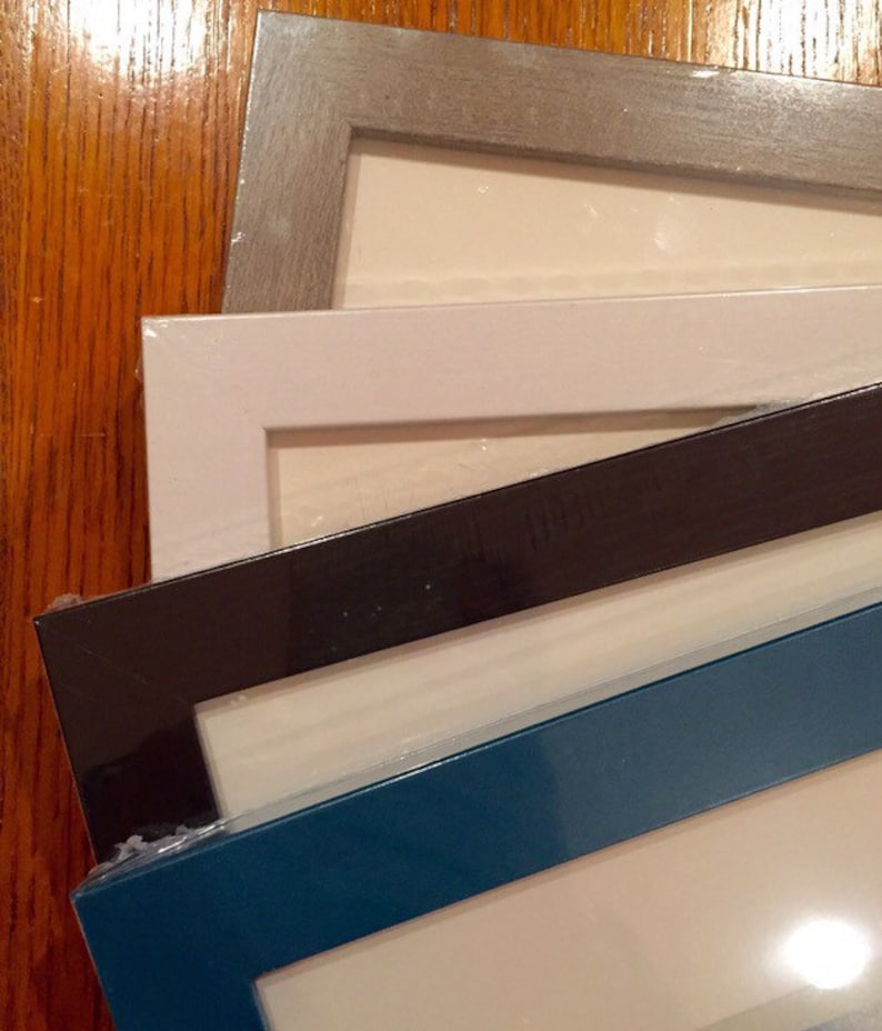 May include: Four picture frames stacked on top of each other. The top frame is a light gray, the second frame is white, the third frame is black, and the bottom frame is a dark teal blue.