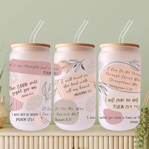 May include: Three pink and white tumblers with inspirational quotes and bible verses. The tumblers have a wood-like lid and a clear straw. The quotes are: "The Lord will fight for me", "I will trust in the Lord with all my heart", and "I can do all things through Christ who strengthens me".