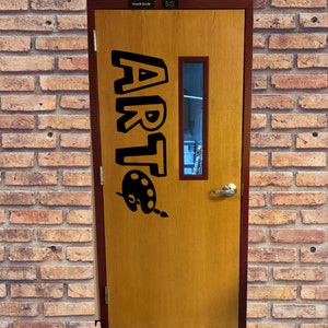 May include: A wooden door with a brown paint finish. The door has a black sign that says "ART" with a paint palette and brush underneath. The door has a small window with a view of a room.