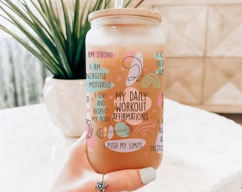 May include: A glass jar with a wooden lid and a straw, filled with a light orange liquid. The jar has a colorful design with the text "My Daily Workout Affirmations" and phrases like "I am strong", "I love and respect my body", and "I push my limits".