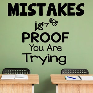 May include: A green wall with the text "MISTAKES are PROOF You Are Trying" written in black. Two wooden desks with notebooks and pencils are in front of the wall.