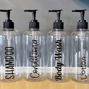 May include: Four clear plastic pump bottles with black pump tops and black labels. The labels read "Shampoo", "Conditioner", "Body Wash", and "Lotion".