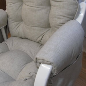 以下が含まれることがあります： 薄いグレーの布地で覆われたクッションとアームレストが付いた白いグライダーロッキングチェア。椅子はパッド入りの背もたれと座席があります。