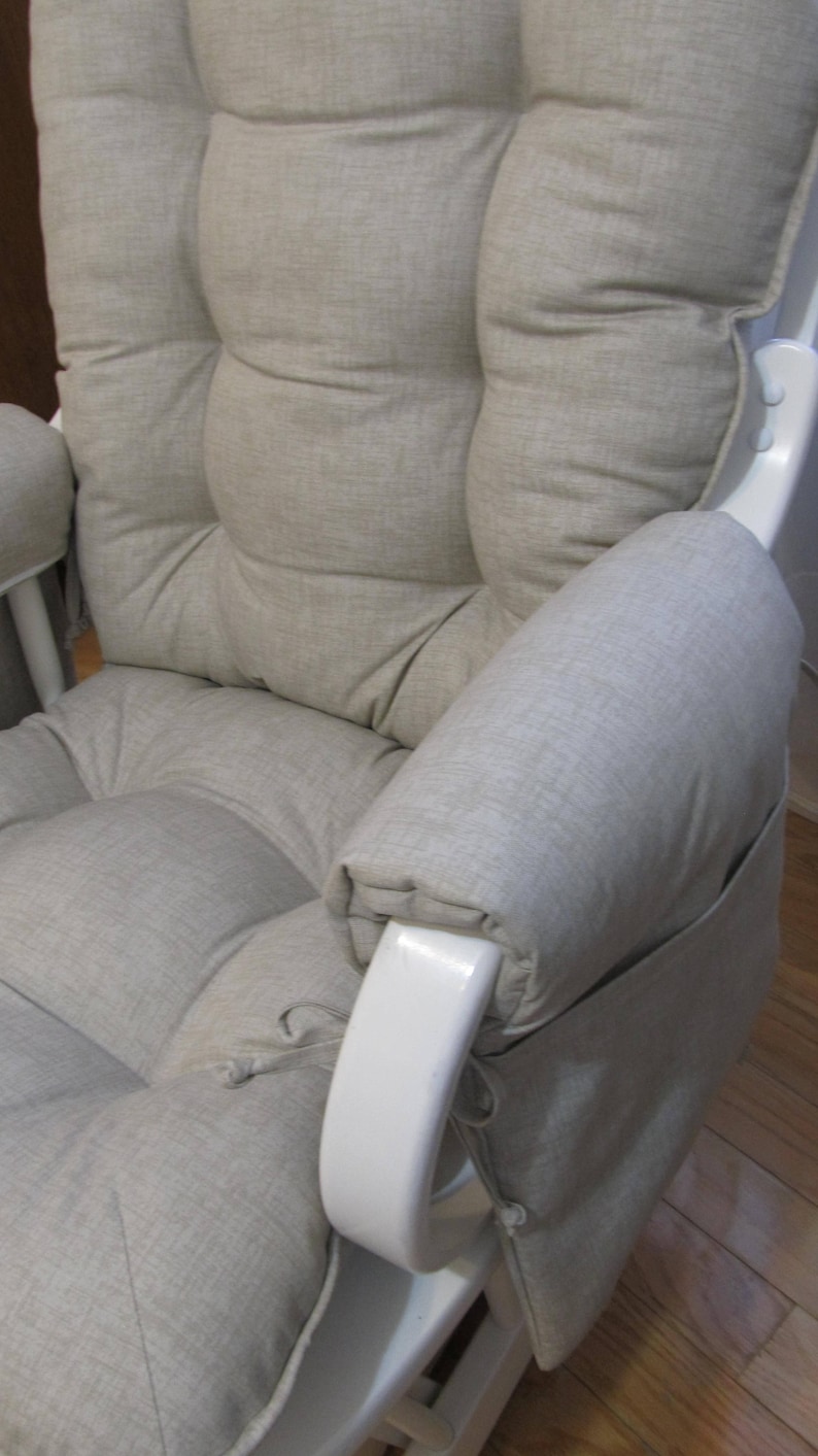 以下が含まれることがあります： 薄いグレーの布地で覆われたクッションとアームレストが付いた白いグライダーロッキングチェア。椅子はパッド入りの背もたれと座席があります。