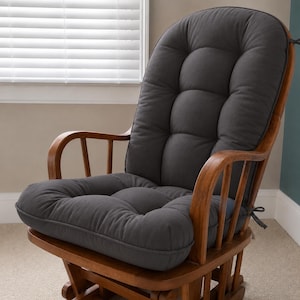 May include: A wooden rocking chair featuring a dark gray, tufted, one-piece cushion that covers the backrest and seat. The cushion is secured to the wooden frame with thin fabric ties on the sides, and the chair has curved armrests and rockers.