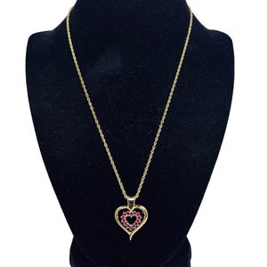 May include: A gold chain necklace with a heart-shaped pendant. The pendant is made of gold and has a red heart in the centre.