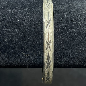 May include: A silver bangle bracelet with a geometric design. The bracelet is made of metal and has a polished finish.