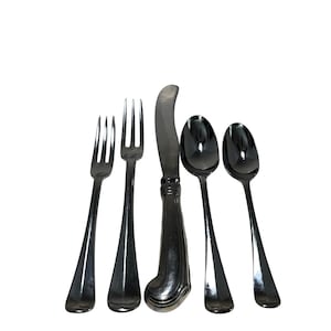 May include: A set of five silver-colored utensils: two forks, a knife, and two spoons. The knife has a curved blade and a decorative handle. The forks have three tines each. The spoons have oval bowls. All utensils have a shiny, reflective surface.