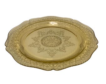 May include: A gold-colored, oval-shaped serving tray with an ornate, embossed design. The tray features a central floral pattern surrounded by detailed scrollwork and a scalloped edge. The tray is made of metal.