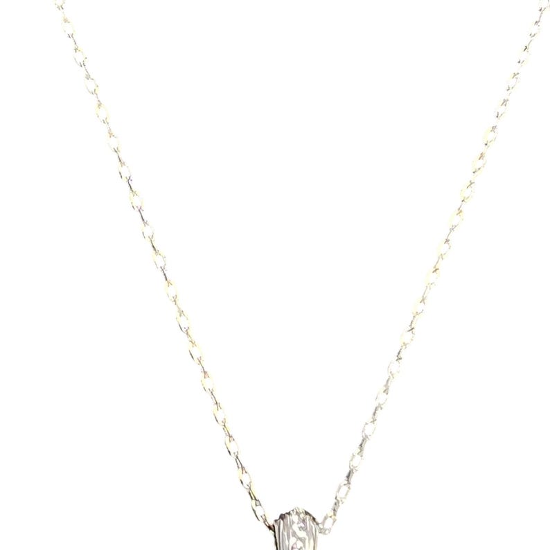 May include: A silver necklace featuring a fine chain and a small, textured pendant. The pendant has a detailed design. The necklace is shown against a white backdrop, emphasizing its understated elegance.