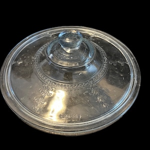 May include: Clear glass lid with a decorative etched design around the edge. The lid has a raised center knob.