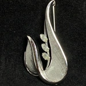 May include: A silver-toned brooch in the shape of a stylized flower with three clear rhinestones.