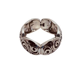 以下が含まれることがあります： 渦巻き模様が細かく施されたシルバーのブレスレット。小さな透明な石が散りばめられている。