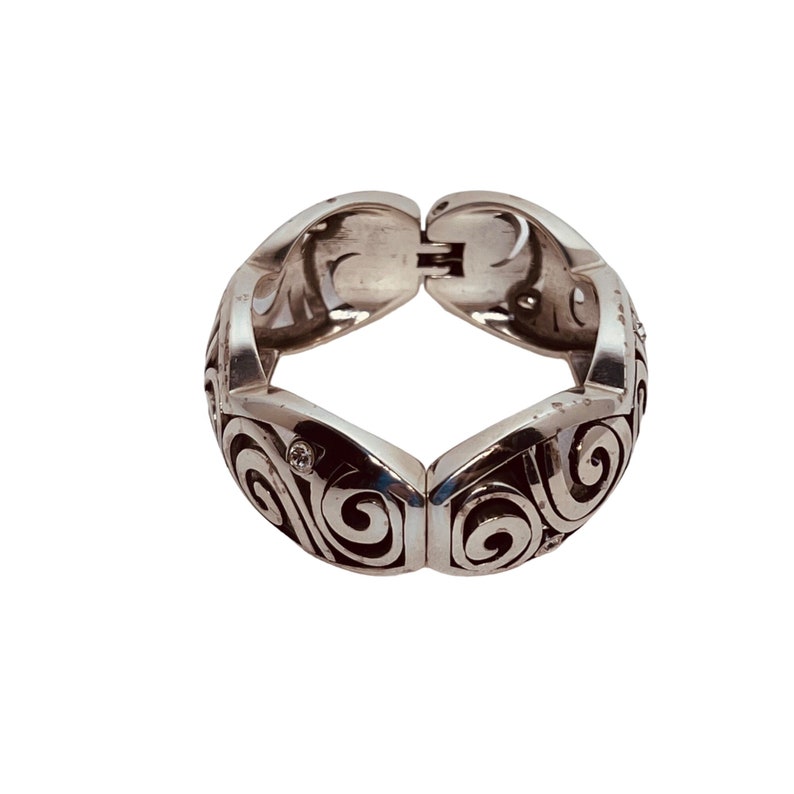 以下が含まれることがあります： 渦巻き模様が細かく施されたシルバーのブレスレット。小さな透明な石が散りばめられている。