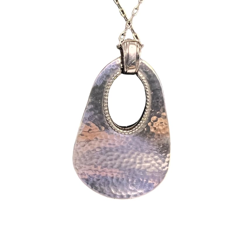 May include: Silver pendant necklace. The pendant has a hammered texture and an oval shape with a central opening. The necklace chain is also silver. The pendant is approximately 5 cm in length.