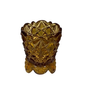 May include: A small, amber-colored glass dish with a scalloped rim and a starburst pattern. The dish has a footed base.