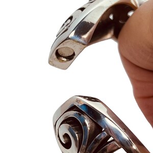 以下が含まれることがあります： 渦巻き模様のシルバーブレスレット。ブレスレットは開いており、磁気留め具が付いています。