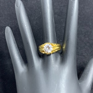 May include: A gold ring with a clear round stone set in a textured band.