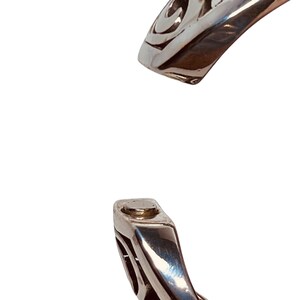 以下が含まれることがあります： ケルトの結び目のデザインが施されたシルバーブレスレット。ブレスレットは開いており、マグネット式の留め具が付いています。