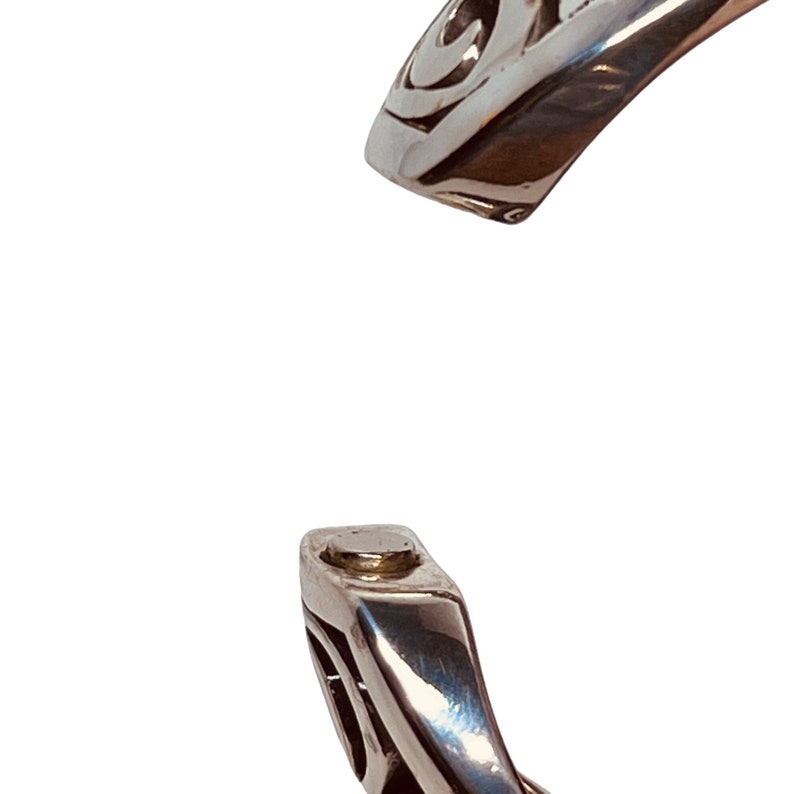 以下が含まれることがあります： ケルトの結び目のデザインが施されたシルバーブレスレット。ブレスレットは開いており、マグネット式の留め具が付いています。