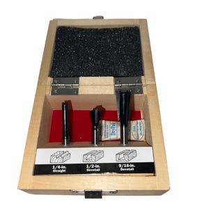 May include: A set of three dovetail router bits in a wooden box. The bits are 1/4-inch straight, 1/2-inch dovetail, and 9/16-inch dovetail. The box is labeled with the size and type of each bit.