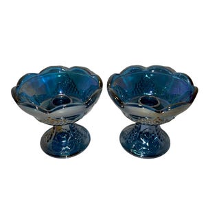 Puede incluir: Un par de candelabros de vidrio azul iridiscente con un diseño de vid. Los candelabros tienen un borde festoneado y una base de pedestal.