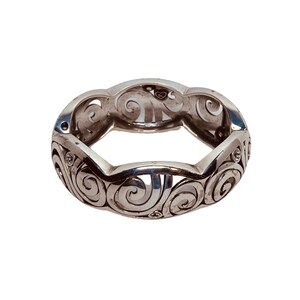 以下が含まれることがあります： 渦巻き模様と小さな透明な石が付いた銀のリング。リングは開いており、内側にハートのチャームが付いています。