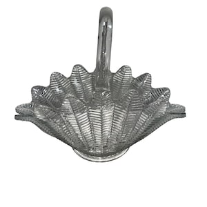 Op de afbeelding: Een heldere glazen mand met een handvat. De mand heeft een schelpachtig ontwerp met een getextureerd oppervlak. De handgreep is gebogen en glad en de mand staat op een ronde basis. Het algehele ontwerp is elegant en decoratief.