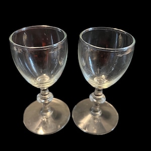 May include: Two clear glass stemmed drinking glasses with a wide bowl and a round base.