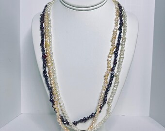 Puede incluir: Exhibición de tres hilos de collares de perlas en varios colores: blanco, crema y gris oscuro. Los collares están colocados sobre un busto blanco, mostrando su longitud y diseño. Las perlas parecen pequeñas y de forma irregular.