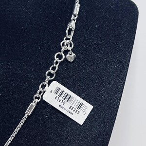 May include: A silver necklace with a fine chain and a heart-shaped charm. The necklace is shown against a black background, with a white tag attached that reads "Made in Taiwan" and includes a barcode.