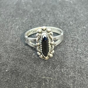 May include: A silver ring featuring a black oval gemstone set in an ornate silver bezel. The ring has a split shank.