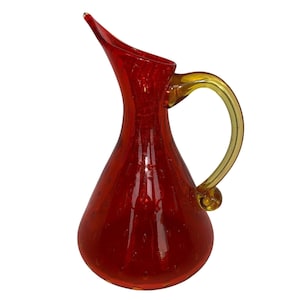 May include: A red glass pitcher with a yellow handle. The pitcher has a textured surface and a round body.