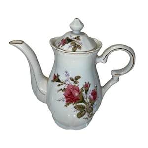 May include: White porcelain teapot with a floral design featuring pink roses and green leaves. The teapot has a lid with a gold trim and a gold handle.