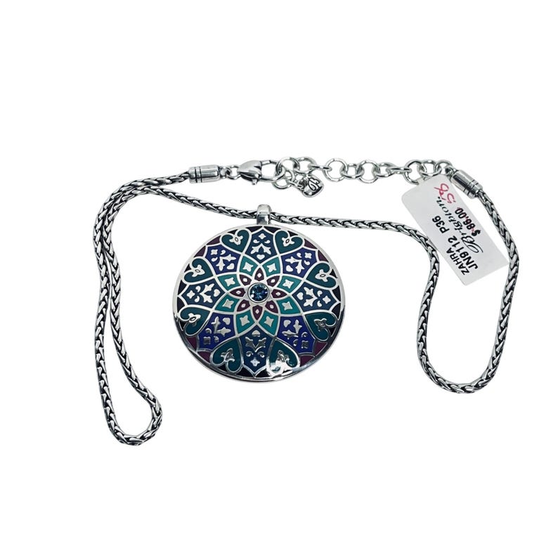 May include: A silver necklace with a circular pendant. The pendant has a detailed design in teal, blue, and purple enamel, with a small blue gemstone in the centre. The necklace has a chain-link style. The pendant is approximately 3 cm in diameter.