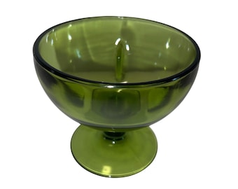 May include: A green glass sundae dish with a rounded bowl and a pedestal base. The dish has a smooth, glossy finish and a small, vertical divider in the center. The color is a vibrant, transparent green.