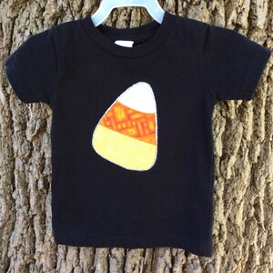 Op de afbeelding: Zwart T-shirt met een geel, oranje en wit snoepmaisontwerp.