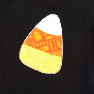 Op de afbeelding: Zwart T-shirt met een geel, oranje en wit snoepmaisontwerp.