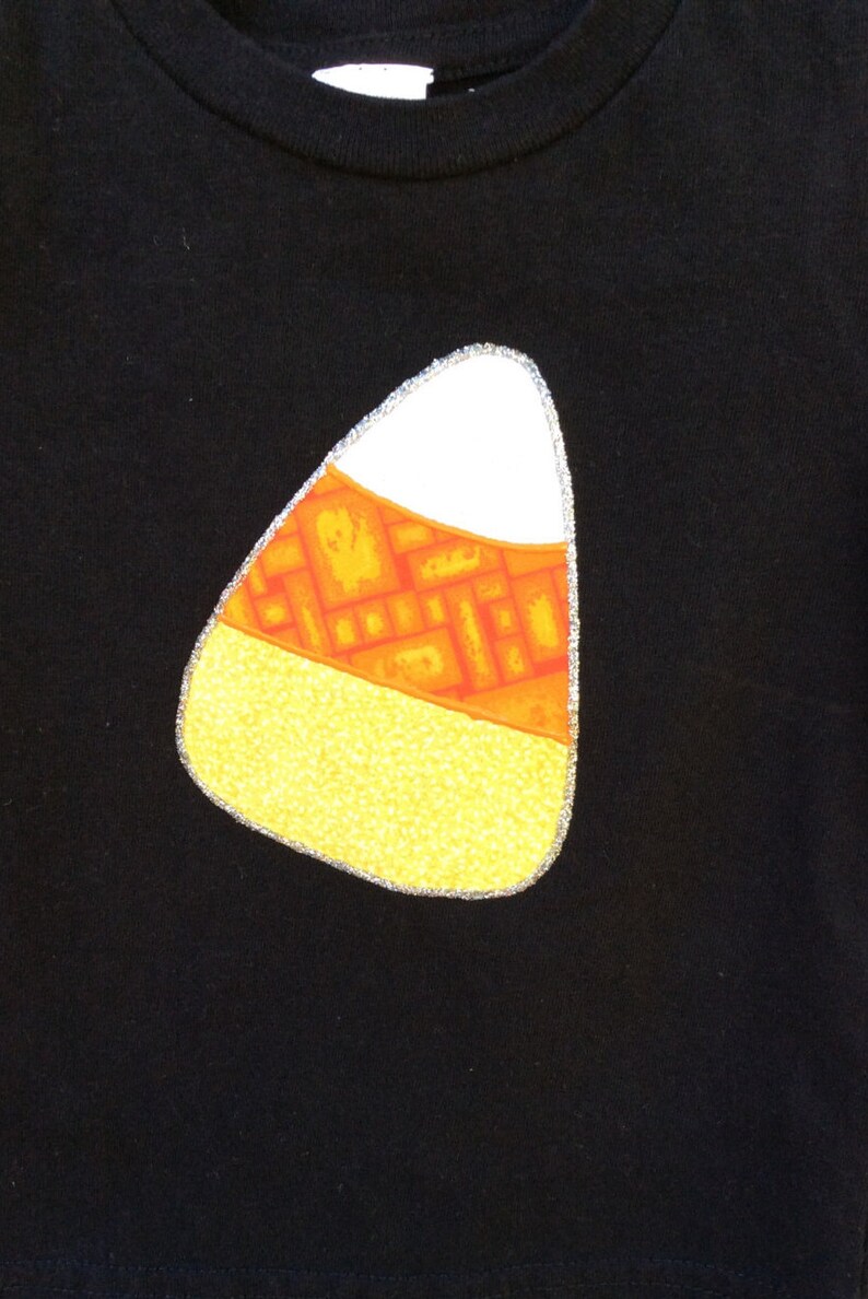 Op de afbeelding: Zwart T-shirt met een geel, oranje en wit snoepmaisontwerp.