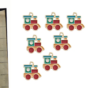 Puede incluir: Seis abalorios de metal de color dorado con forma de tren de juguete. Cada abalorio tiene un diseño de pintura roja, verde y amarilla con un círculo blanco en el centro. Los abalorios tienen un bucle en la parte superior para sujetarlos a un collar o pulsera.