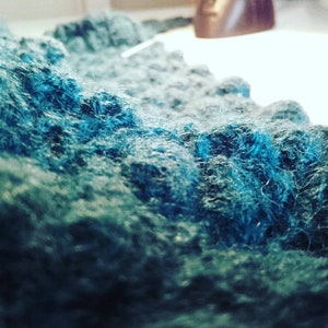 Puede incluir: Primer plano de una tela suave y peluda en tonos de azul verdoso y azul. La tela tiene una textura casi como de nube.