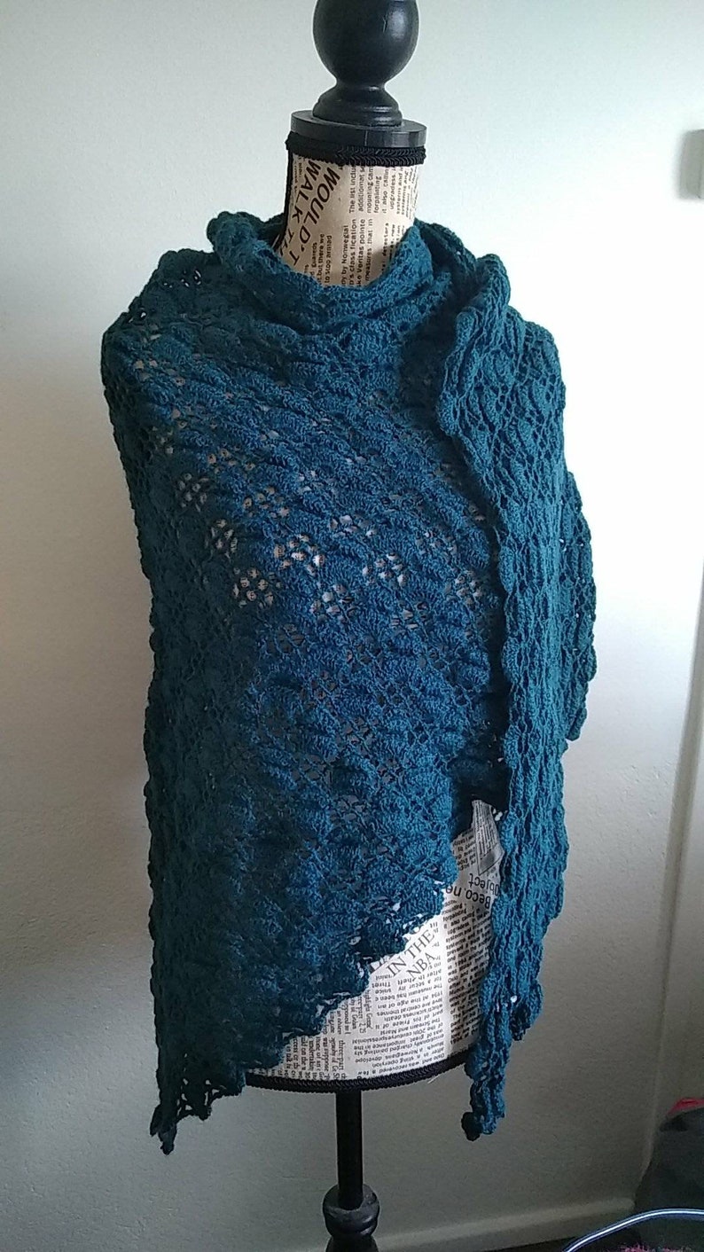 Puede incluir: Chaleco de ganchillo de color turquesa con un patr&oacute;n de encaje. El chal est&aacute; drapeado sobre un maniqu&iacute;.