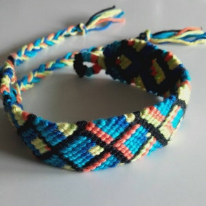 May include: A handmade friendship bracelet with a woven design. The bracelet features a pattern of blue, black, yellow, and coral threads. The braided ties are blue, yellow, and coral. This accessory is perfect for adding a pop of color.