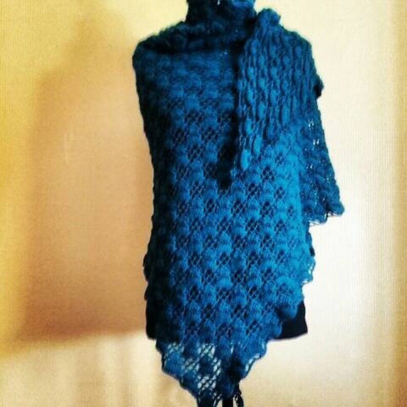 Puede incluir: Un chal de ganchillo azul turquesa con un patr&oacute;n de encaje. El chal est&aacute; drapeado sobre un maniqu&iacute;.