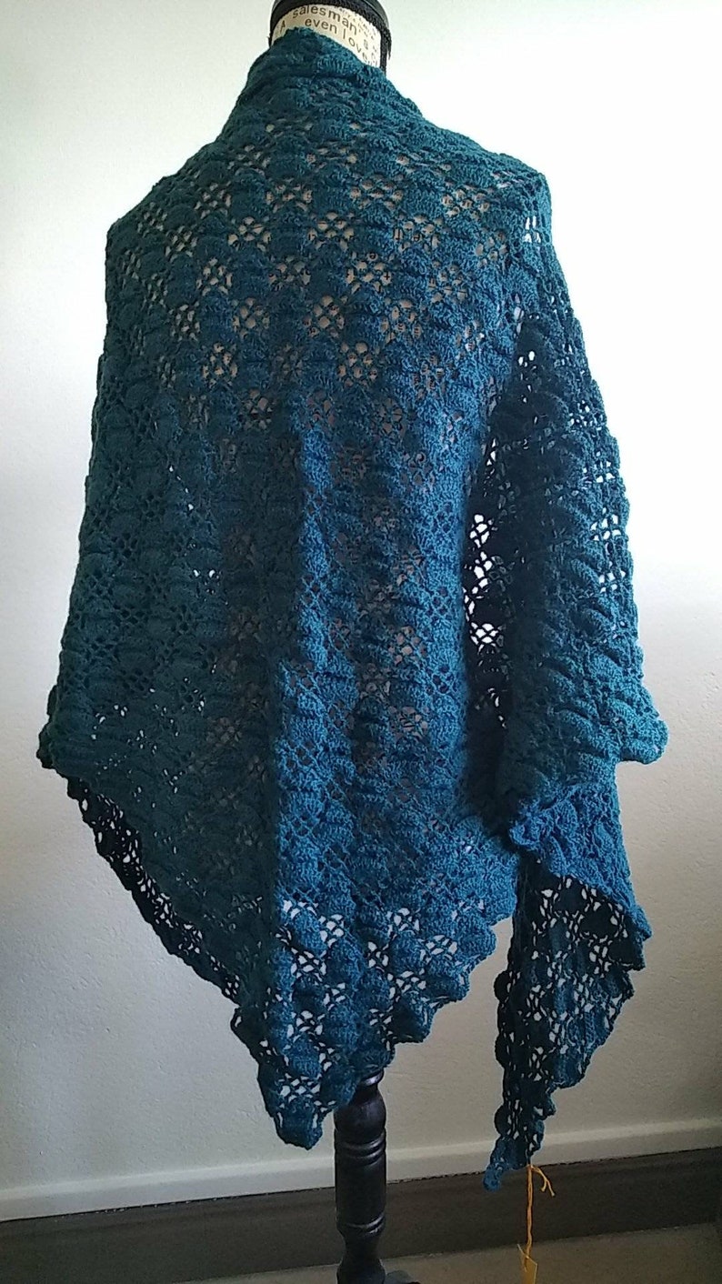 Puede incluir: Chaleco de ganchillo color turquesa con un delicado patr&oacute;n de encaje. El chal est&aacute; drapeado sobre un maniqu&iacute; y tiene un borde con flecos.