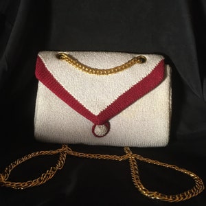 Cartera vintage de punto con correa de cadena bañada en oro. En muy buen estado, con poco uso. Ribete en gris claro y arándano.